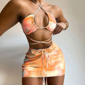 Orange tie-dye two-piece swimwear set with halter bikini top and crisscross back straps, paired with ruched mini skirt and adjustable tie waist.