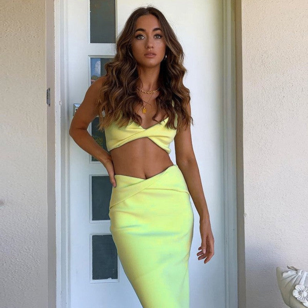 Woman in neon yellow wrap crop top and high-waisted midi skirt set standing in doorway.