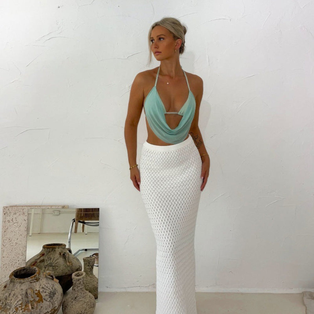 Model wearing a light mint green halter crop top with draped cowl neckline and front cutout detail, paired with a long white crochet skirt.