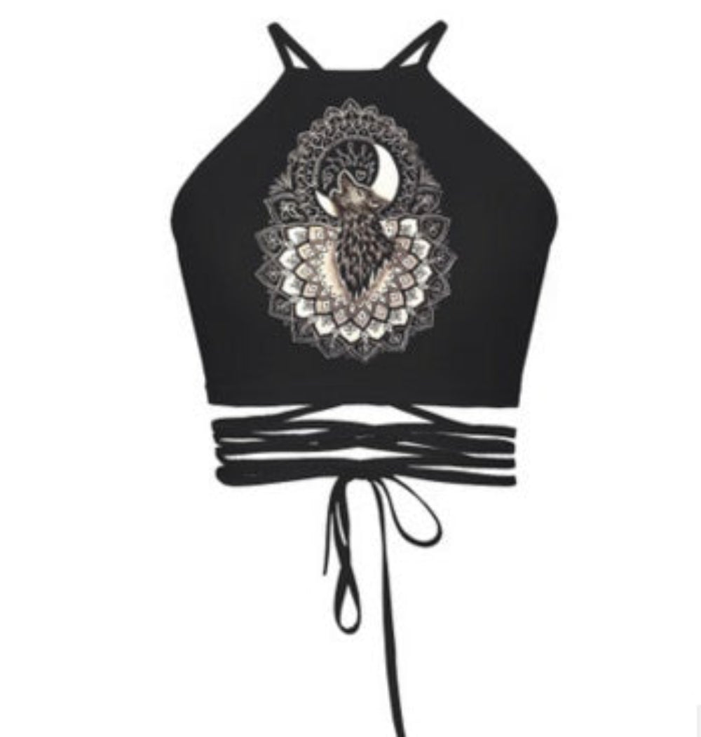 Black halter crop top with wolf and moon mandala graphic print and multi-strap tie-back detail, shown flat lay on white background.