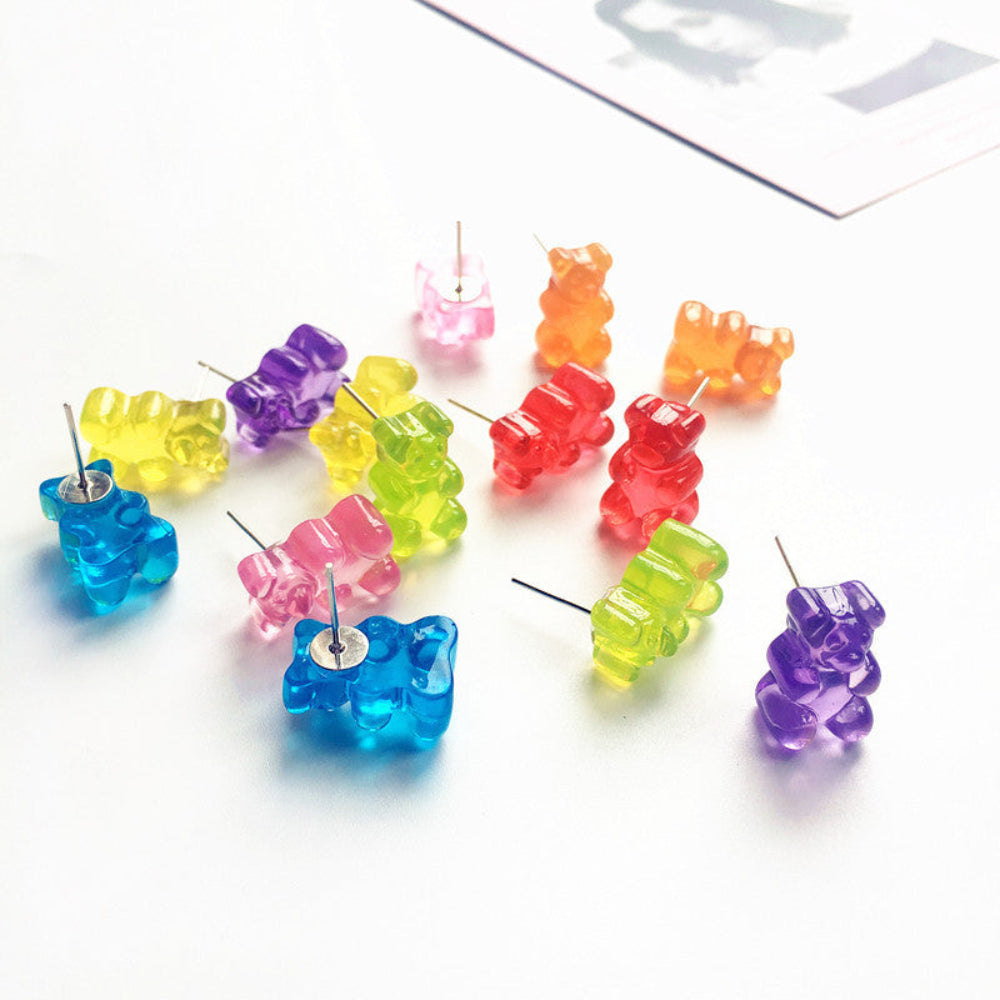 Set of fun translucent gummy bear stud earrings in vibrant rainbow colors including blue, purple, yellow, green, pink, orange, and red, scattered on white background