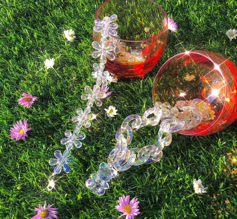 Transparent floral acrylic bracelet on grass with flowers – trendy clear flower link chain bracelet, outdoor lifestyle product photo.