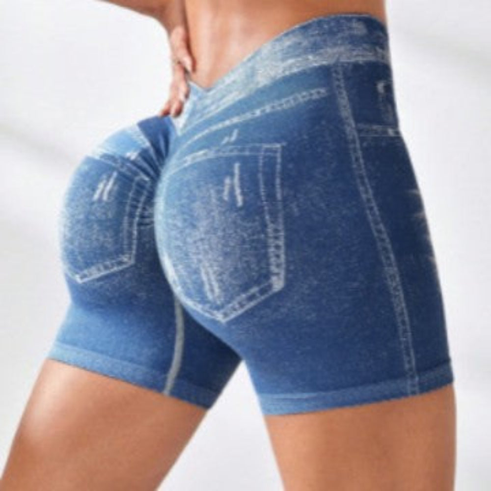 Woman modeling blue denim-style high-waisted stretch shorts with back pockets and white contrast stitching, shown from a rear three-quarter view against a plain studio background.