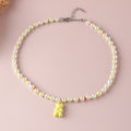 White pearl yellow gummy bear necklace – trendy colorful beaded choker with fun bear pendant, studio pink background.