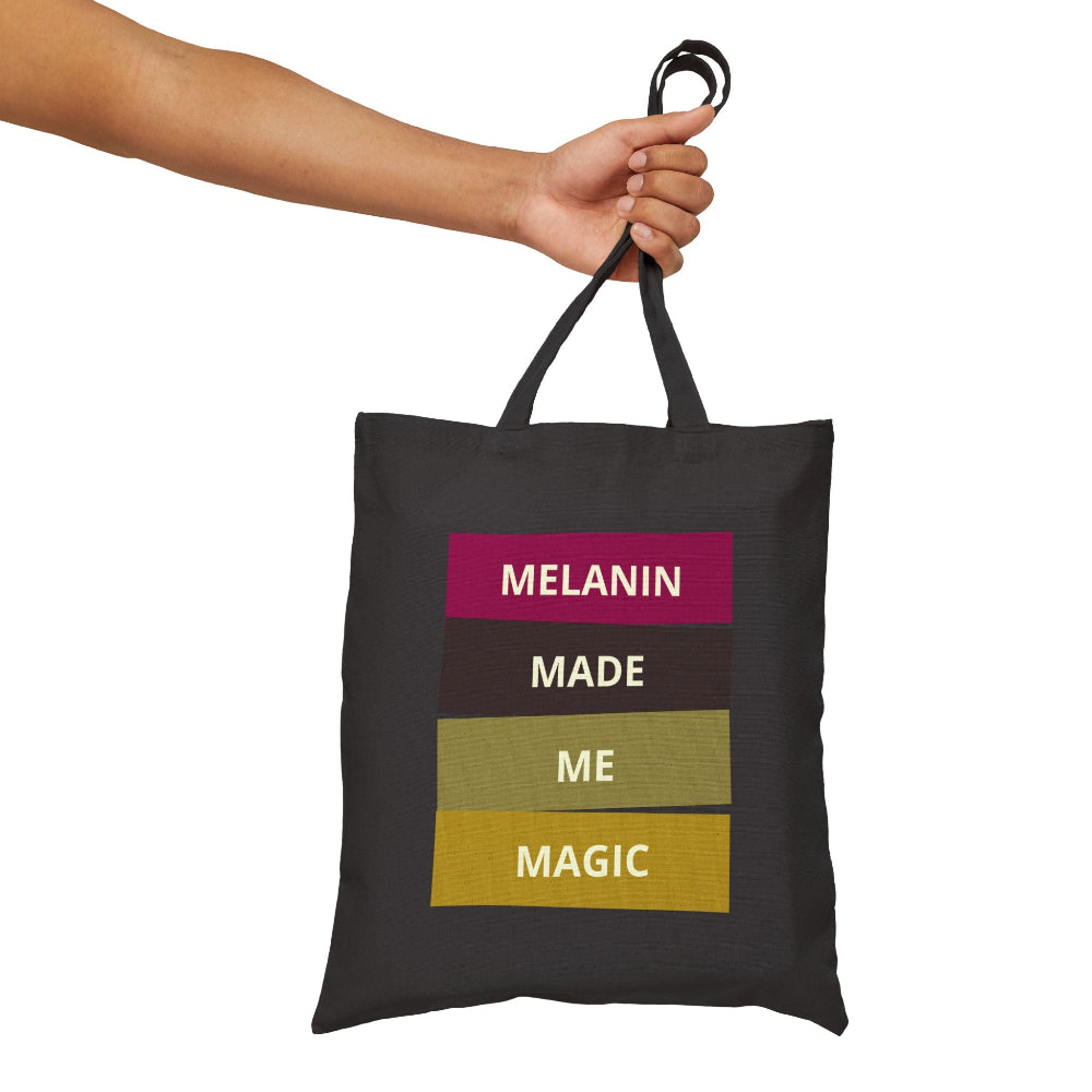 Hand holding black canvas tote bag with "MELANIN MADE ME MAGIC" graphic