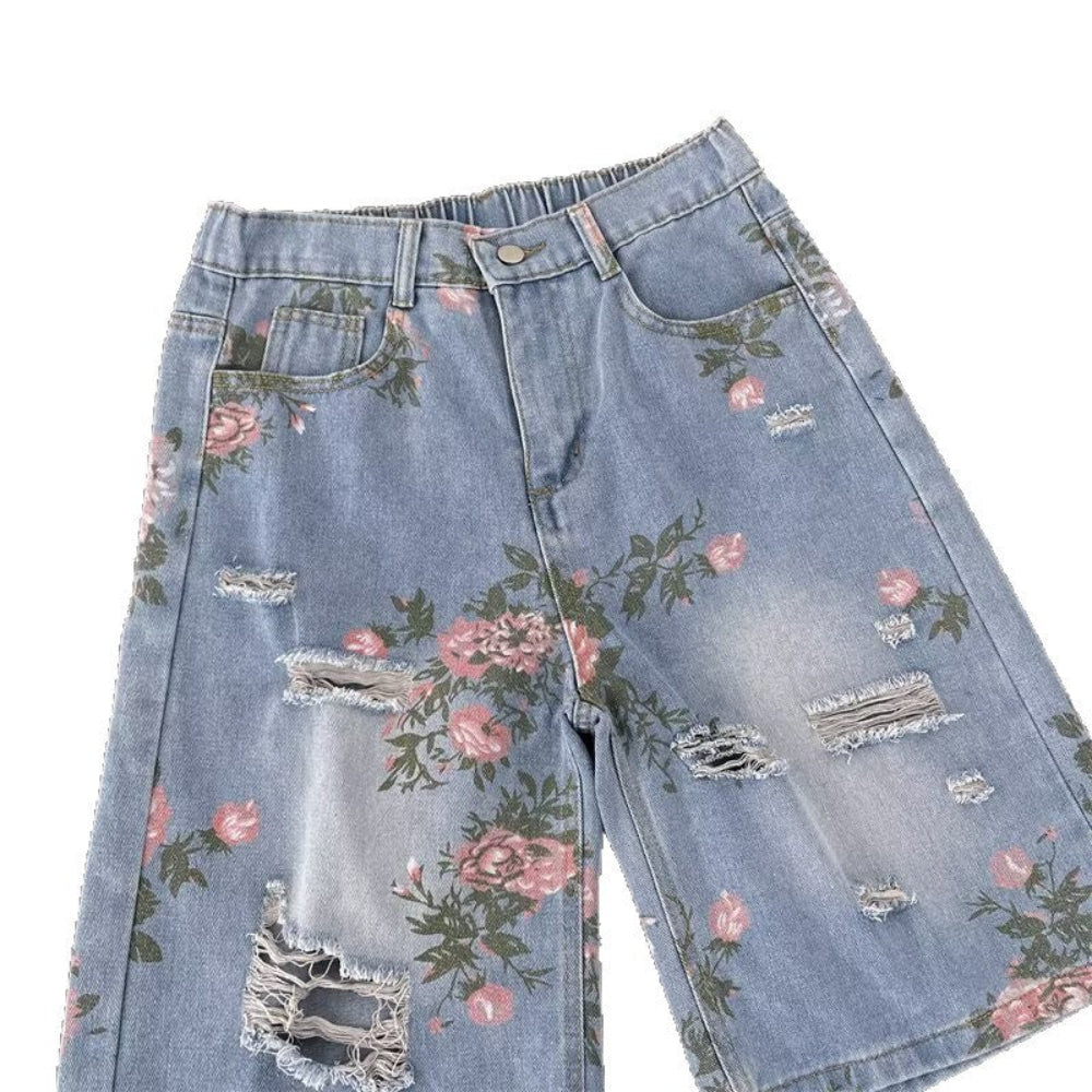 Light blue distressed denim shorts featuring pink floral rose prints, frayed rips, and raw hems, shown in a detailed product view. Stylish vintage-inspired fashion piece for Boutique Jolie.