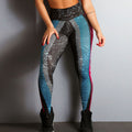 Woman modeling black and blue geometric patterned high-waisted leggings with pink side accents, shown from a three-quarter rear view with hands on thighs, paired with black sneakers against a plain studio background.