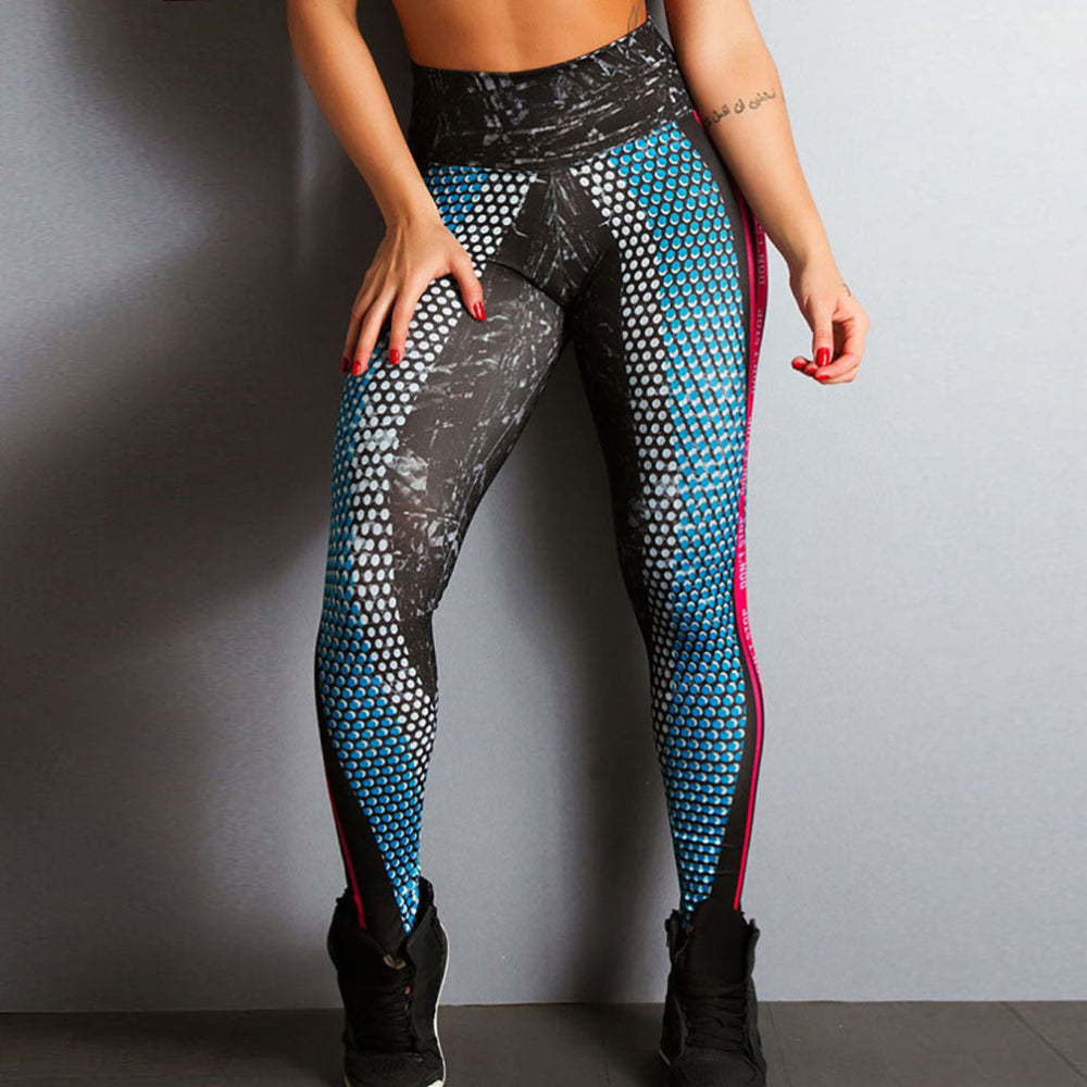 Woman modeling black and blue geometric patterned high-waisted leggings with pink side accents, shown from a three-quarter rear view with hands on thighs, paired with black sneakers against a plain studio background.