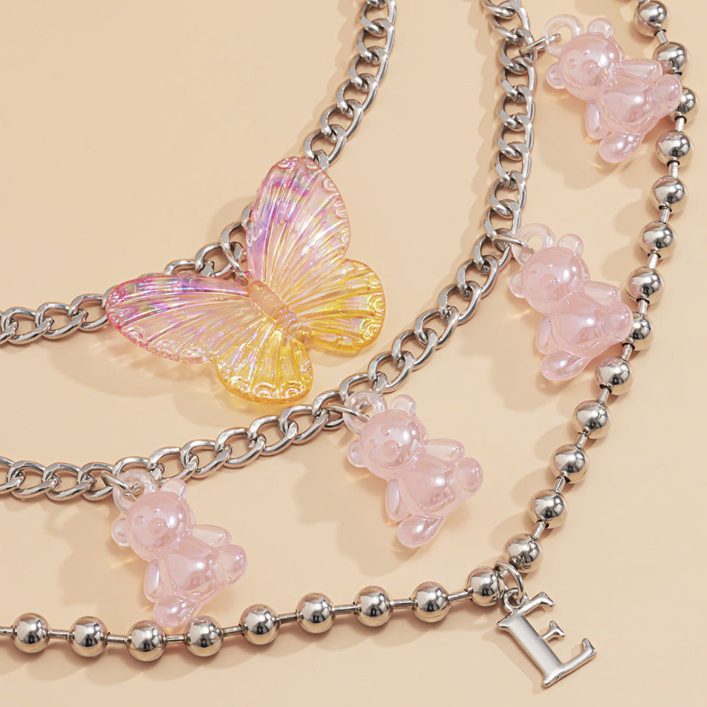 Silver butterfly and teddy bear charm necklaces – trendy layered statement jewelry with pink bear pendants and holographic butterfly, product flat lay.
