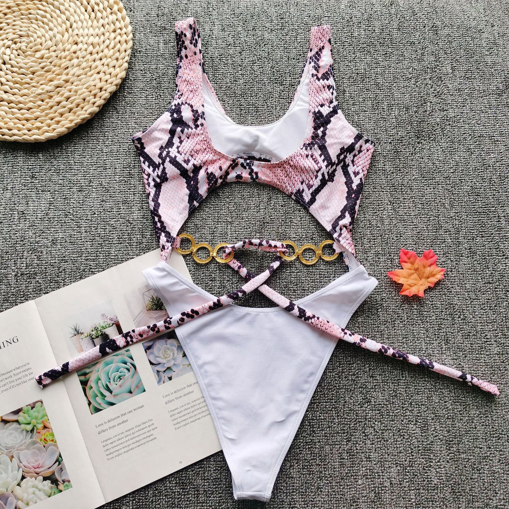 Pink snake print cutout one-piece swimsuit with gold ring detail and tie waist flat lay.