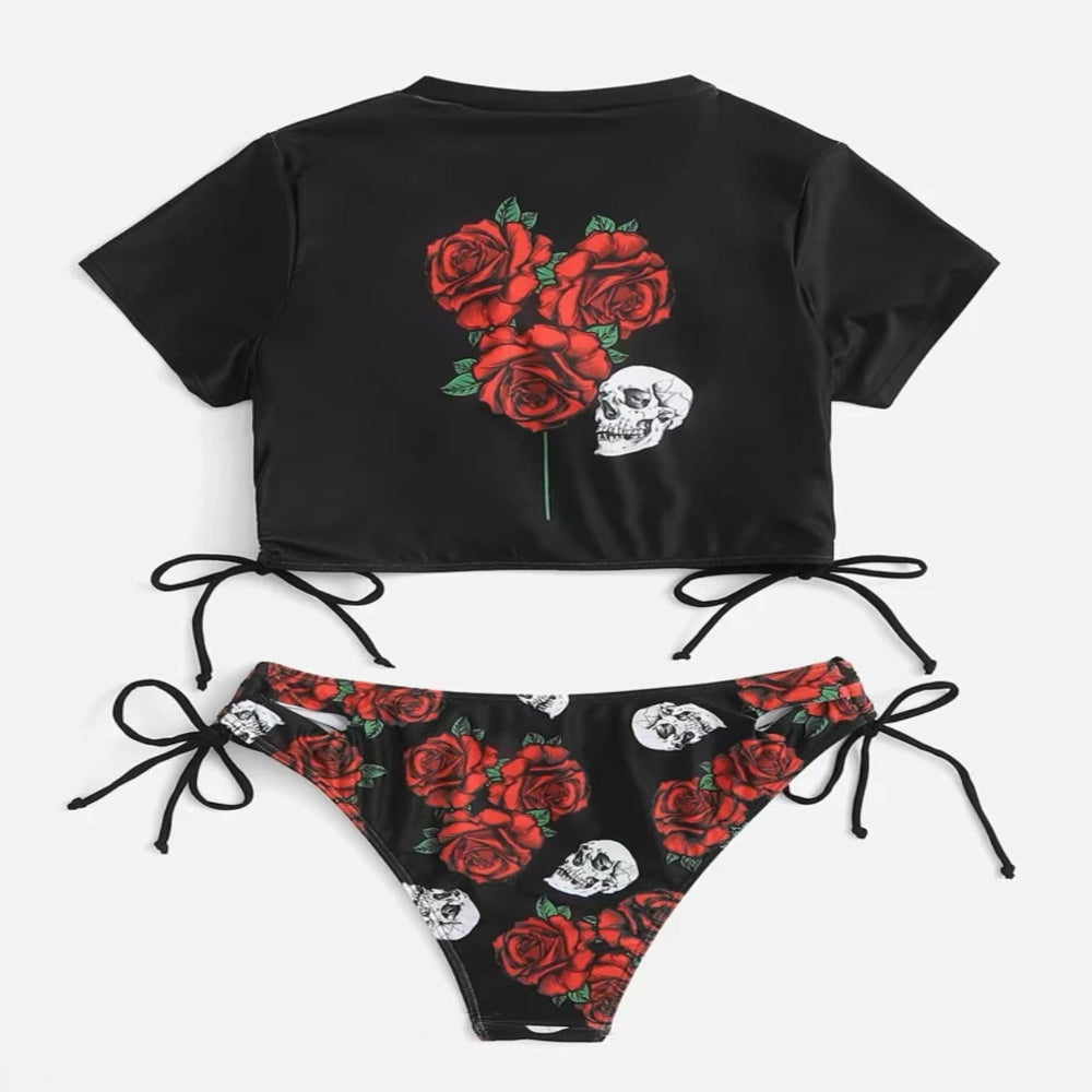 Black crop top with red roses and white skulls, paired with a matching black bikini bottom with floral design on a white background.