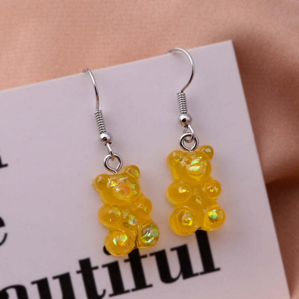 Pair of yellow iridescent gummy bear earrings with silver fishhook ear wires, shown on a white display card