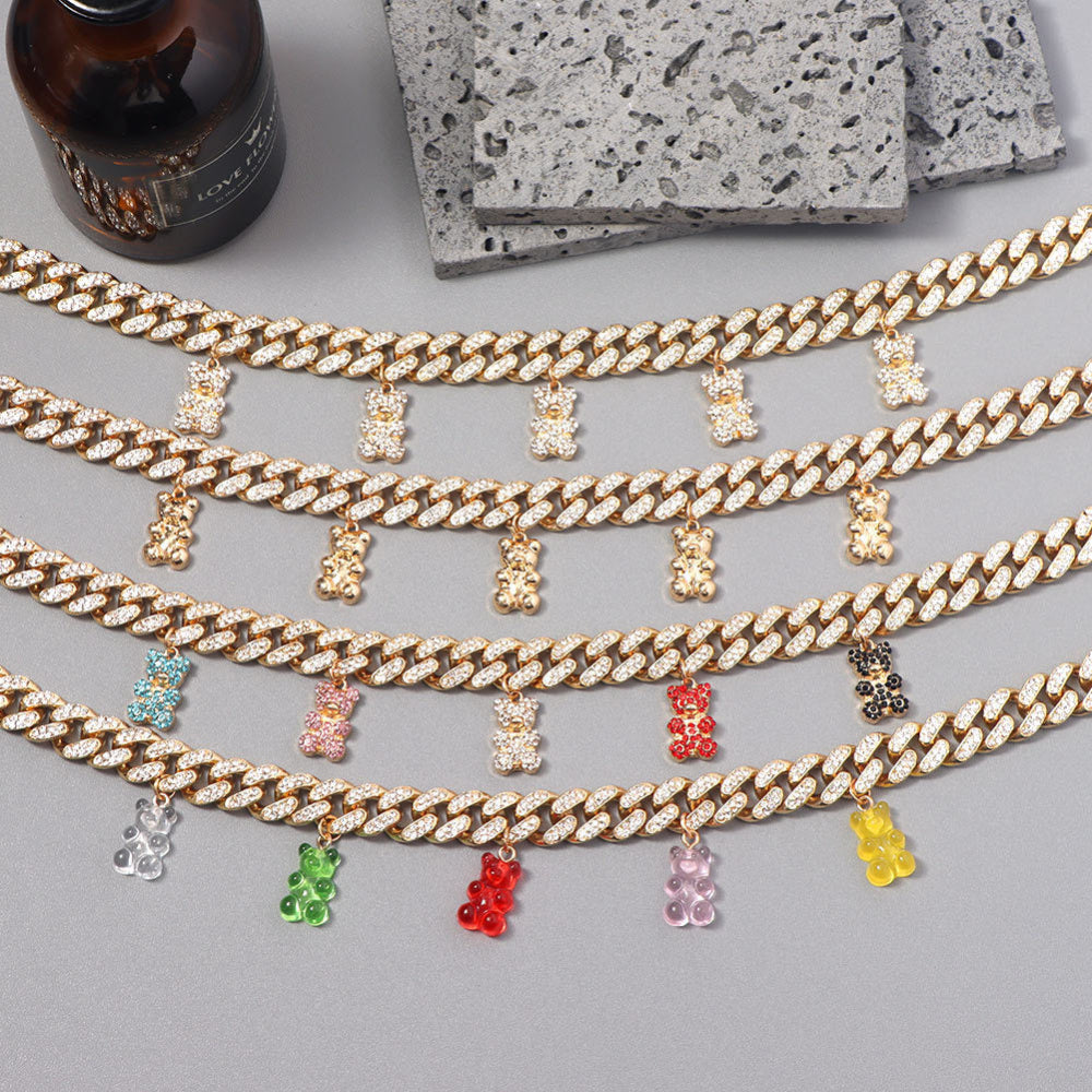 Collection of luxury gold Cuban link choker necklaces fully iced with sparkling cubic zirconia stones, each featuring multiple dangling teddy bear charms in gold, clear, turquoise, pink, red, black, green, and yellow. Bold, glamorous statement pieces displayed together on a neutral surface.