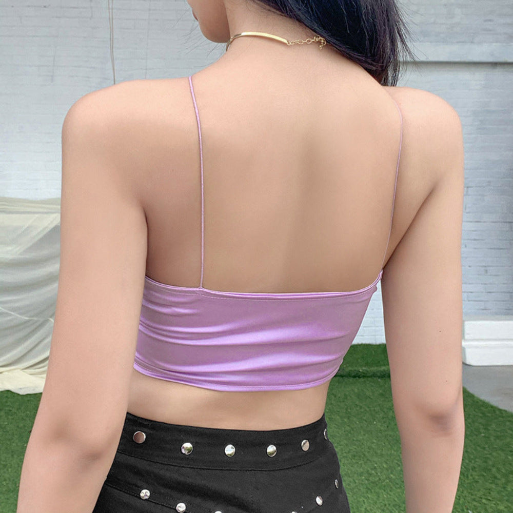  Back view of a woman wearing a shiny lilac satin crop top with delicate spaghetti straps, highlighting the sleek, stretchy fit and flattering open-back design. Styled with black high-waisted studded bottoms.
