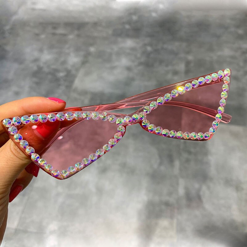 Hand holding pink triangle sunglasses with iridescent rhinestone frames.