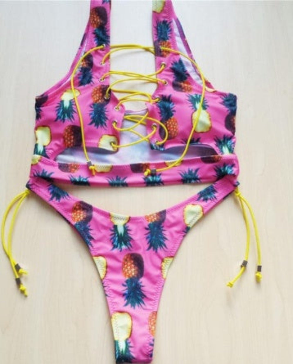 Pink pineapple print bikini set with lace-up halter top and tie-side bottom flat lay.