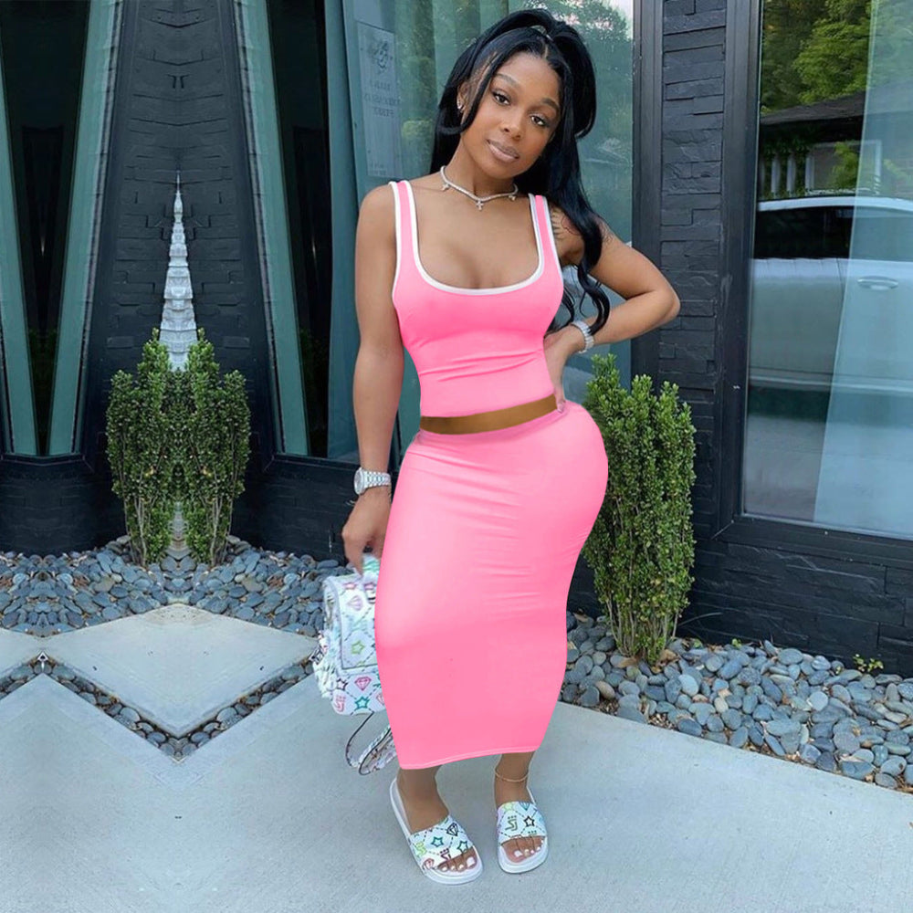 Woman in bright pink sleeveless crop top and high-waisted midi skirt set standing outdoors holding floral handbag.