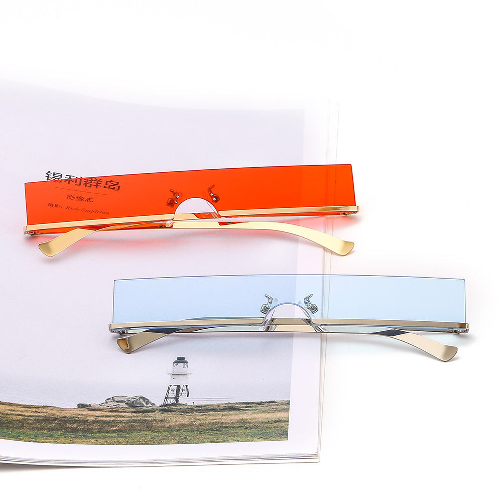 Rimless rectangular sunglasses in orange and light blue with gold temples, styled on a magazine.