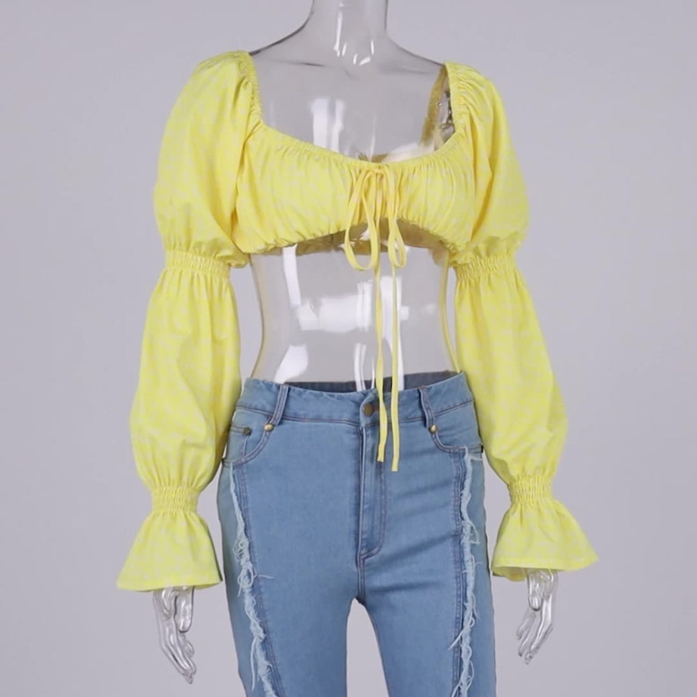 Yellow floral print cropped puff sleeve blouse on a transparent mannequin, featuring a square neckline with ruched elastic, front tie drawstring, and voluminous long sleeves with smocked elastic cuffs. Paired with light-wash distressed denim jeans.