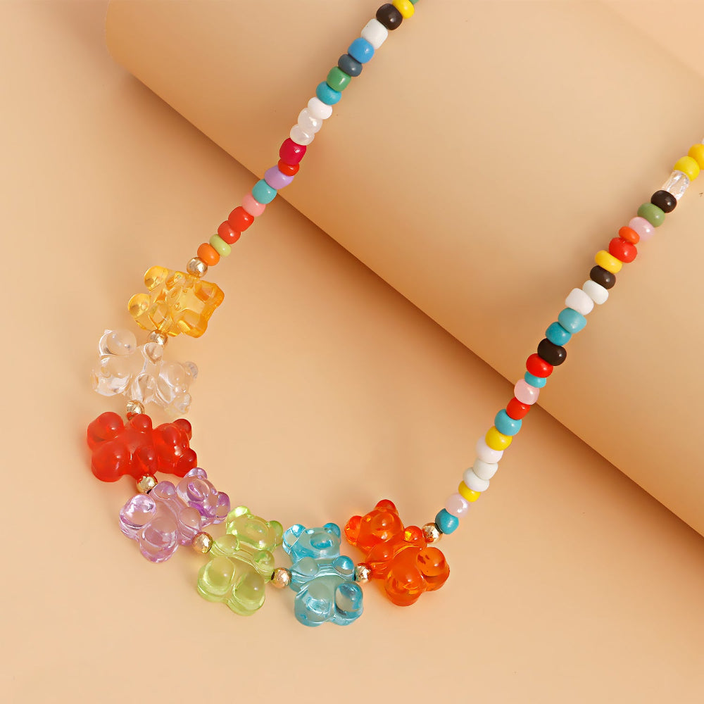 Colorful beaded choker necklace worn on a model, featuring multicolored seed beads and a vibrant row of translucent gummy bear charms in rainbow shades — yellow, clear, red, purple, green, blue, and orange. Playful and eye-catching summer jewelry design.