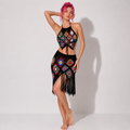 Model with pink hair wearing black crochet halter crop top and matching fringed skirt with colorful granny square patterns.
