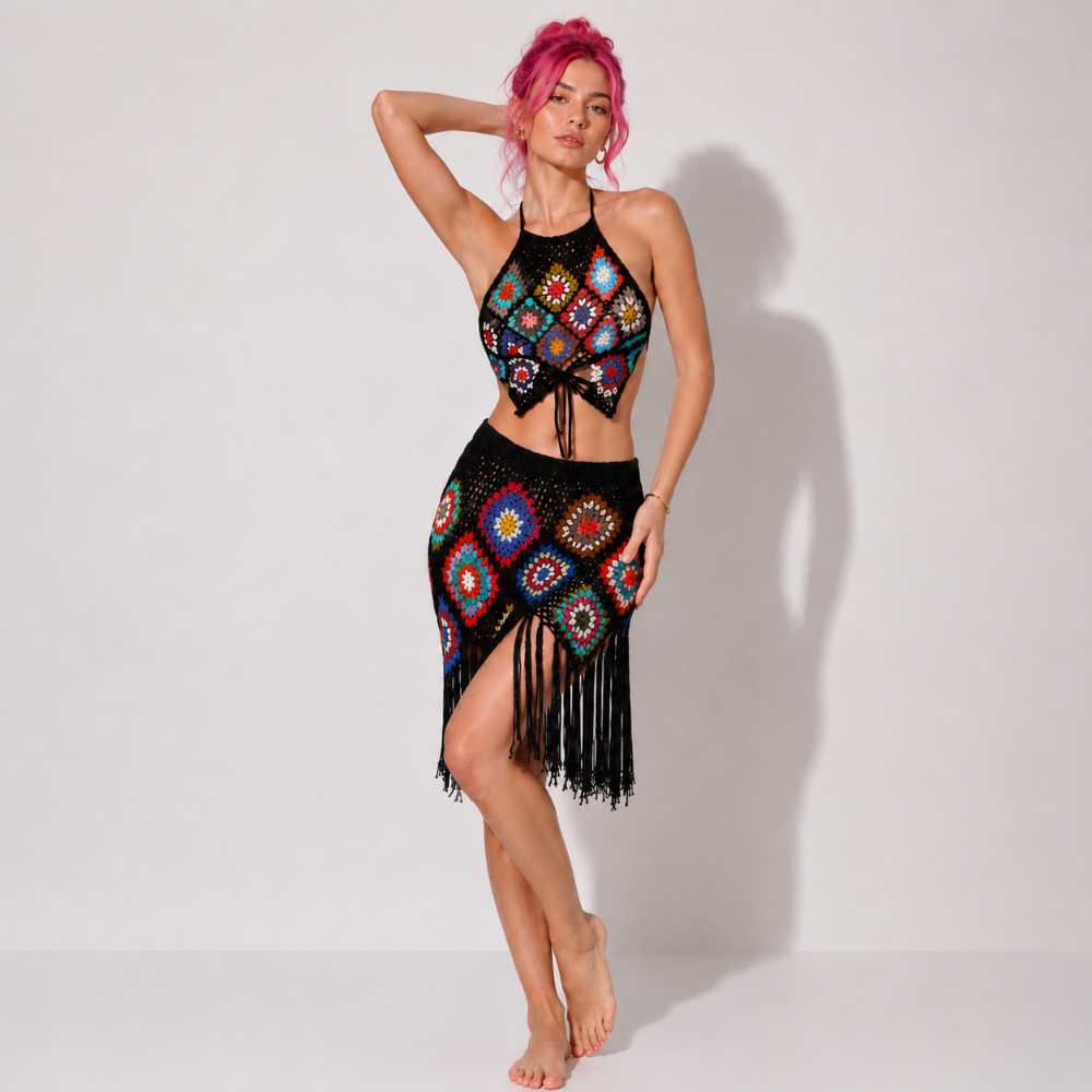 Model with pink hair wearing black crochet halter crop top and matching fringed skirt with colorful granny square patterns.