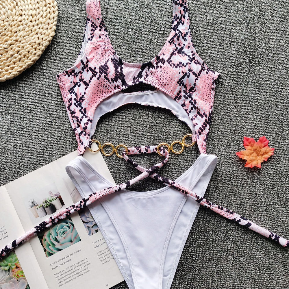 Pink snake print cutout one-piece swimsuit with gold ring detail and tie waist flat lay.