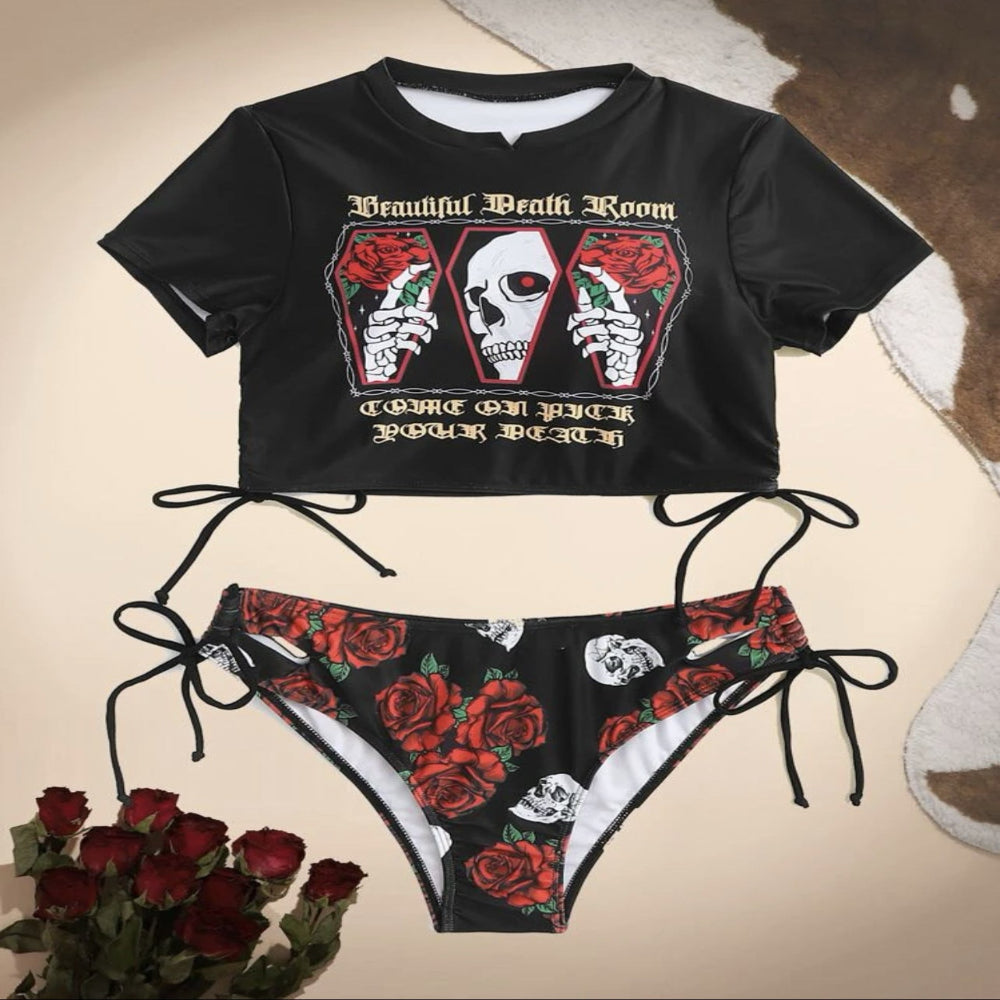 Black crop top and bikini bottom set with skull and rose design on a beige background.
