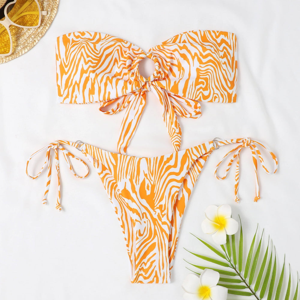 Orange and white patterned bikini set on a white background with flowers and a hat.