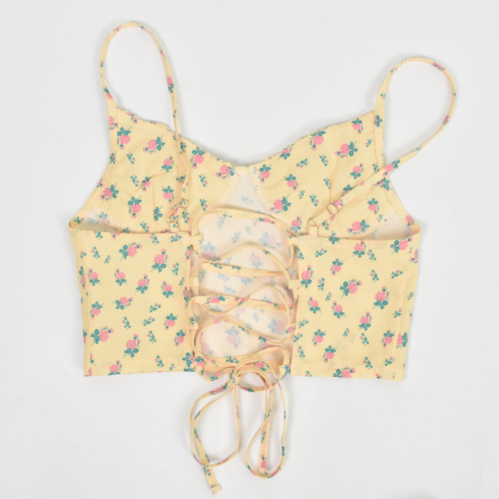 Yellow floral print crop top with lace-up corset back detail and thin spaghetti straps, shown flat lay on white background.