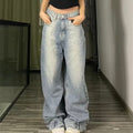 Woman modeling light-wash blue wide-leg baggy jeans with hands in front pockets, paired with a black crop top and white sneakers, standing in a hallway with wooden flooring.
