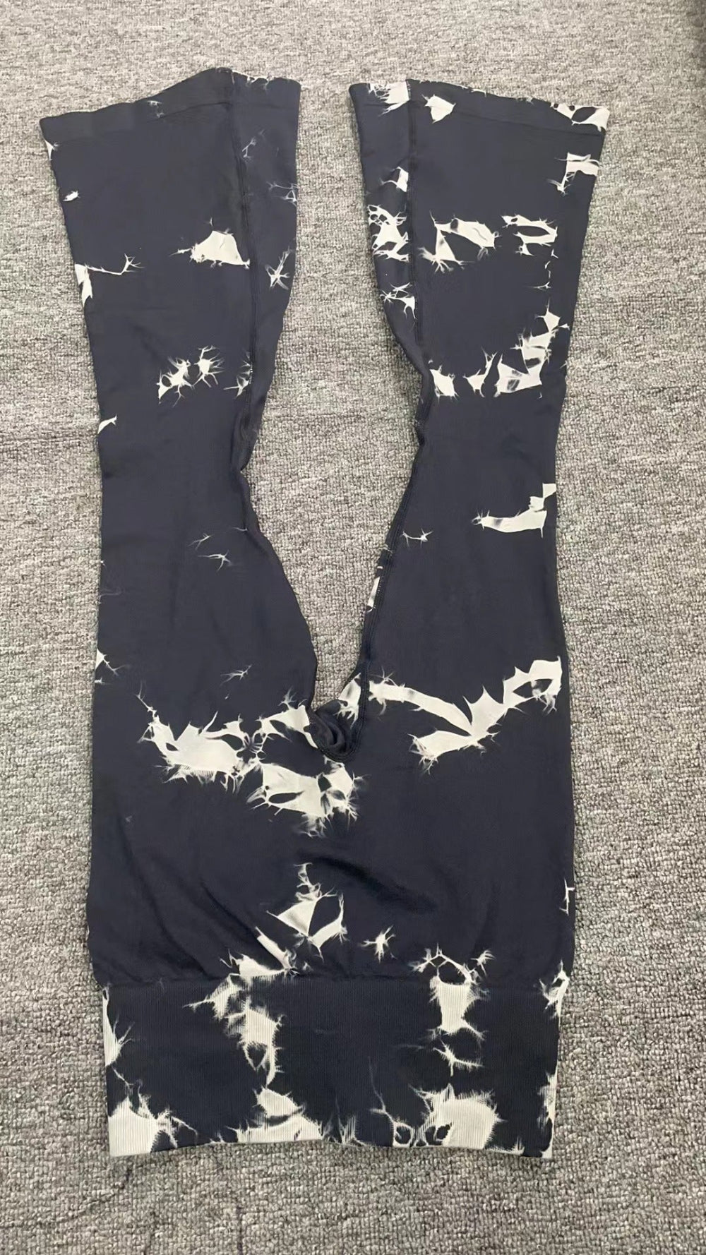 Black leggings with white abstract pattern laid flat on a gray textured surface, showing the full length and waistband details.