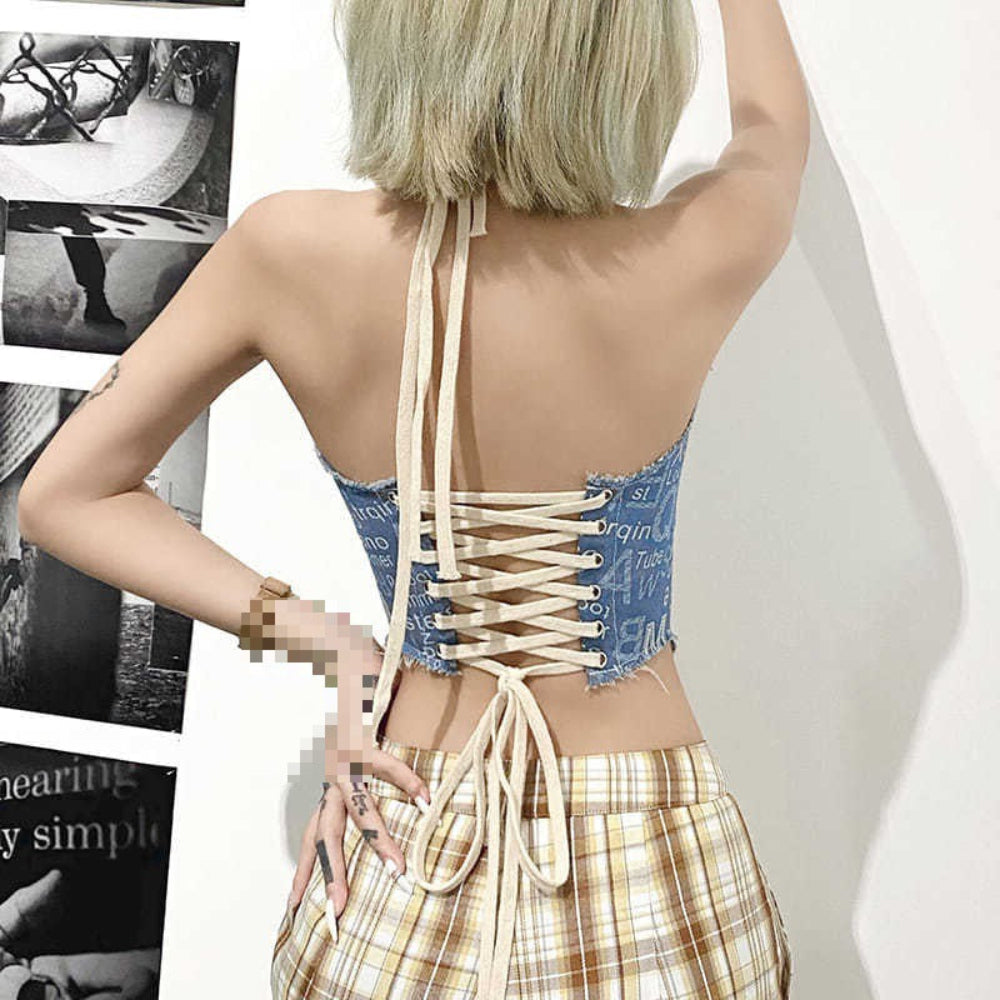 Back view of a woman with blonde bob haircut wearing a blue number print halter crop top with white corset-style lace-up back and long tie strings. Features crisscross lacing and raw hem details, paired with plaid pants.