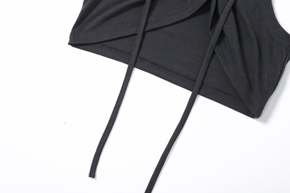 Close-up detail of the lower portion of a black crop top featuring wrapped and twisted fabric construction at the hem with two long adjustable black ties hanging down.