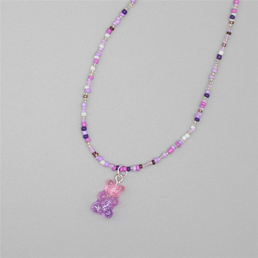 Purple and pink beaded necklace with a soft mix of pastel purple, pink, white, and metallic seed beads paired with a sparkling translucent pink-to-purple ombre gummy bear pendant. Playful single-strand design laid flat on a light gray background, showcasing its sweet and whimsical style.