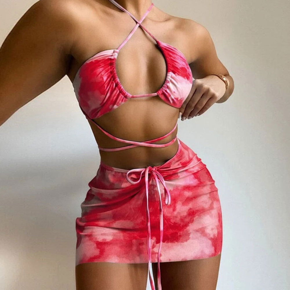 Red tie-dye two-piece swimwear set featuring a halter bikini top with crisscross back straps and a matching ruched mini skirt with adjustable tie waist.