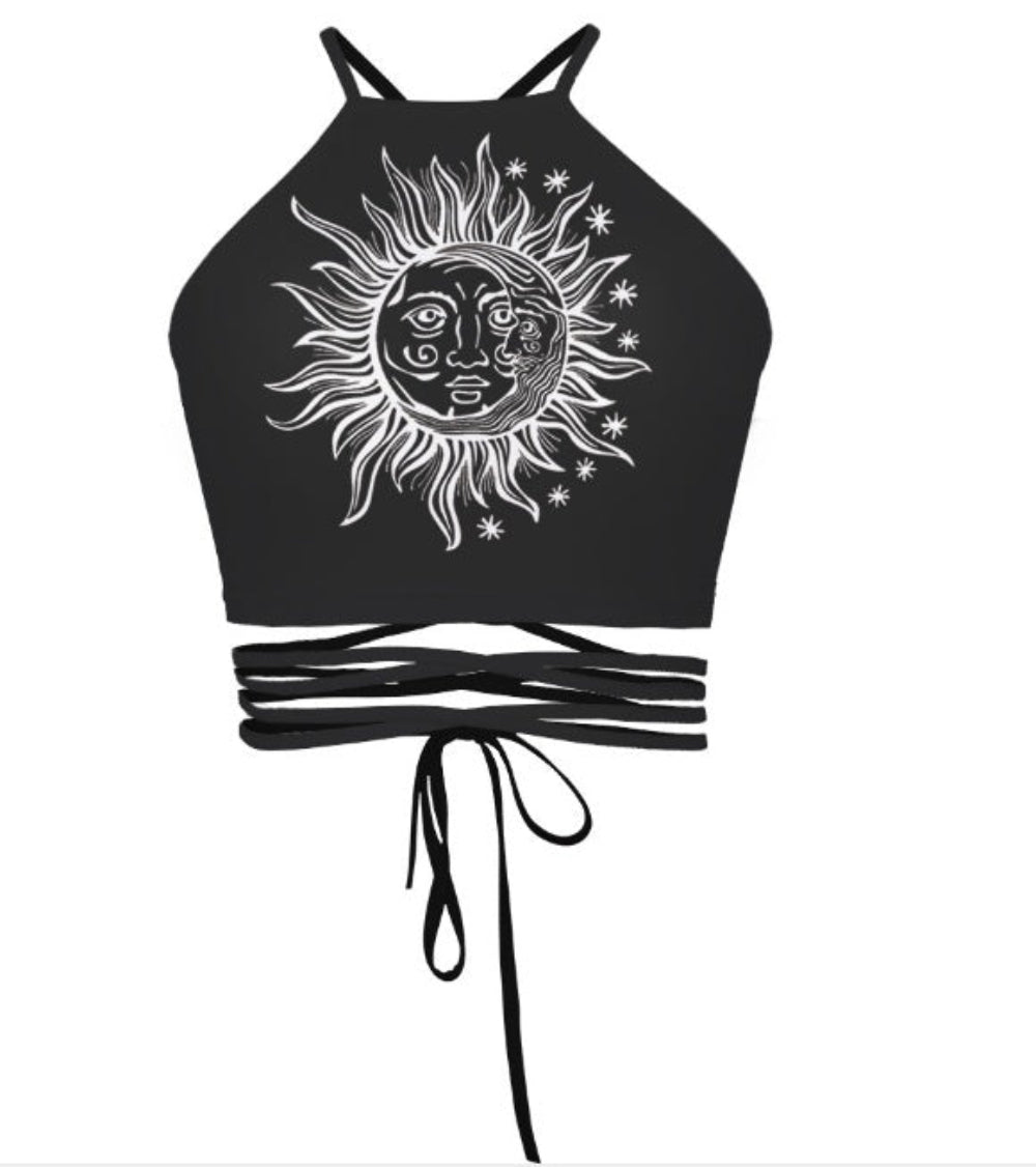 Black halter crop top with celestial sun and moon graphic print and multi-strap tie-back detail, shown flat lay on white background.