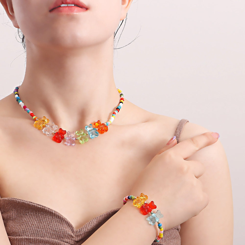 Close-up of a colorful beaded choker necklace worn on a model, featuring multicolored seed beads and a vibrant row of translucent gummy bear charms in rainbow shades — yellow, clear, red, purple, green, blue, and orange. Playful and eye-catching summer jewelry design.