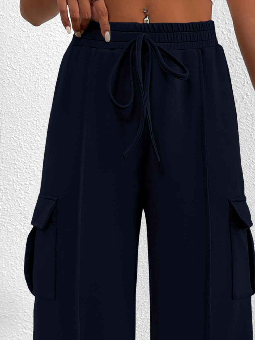 Woman wearing navy blue wide leg cargo pants with drawstring waist and large side pockets against a textured white background