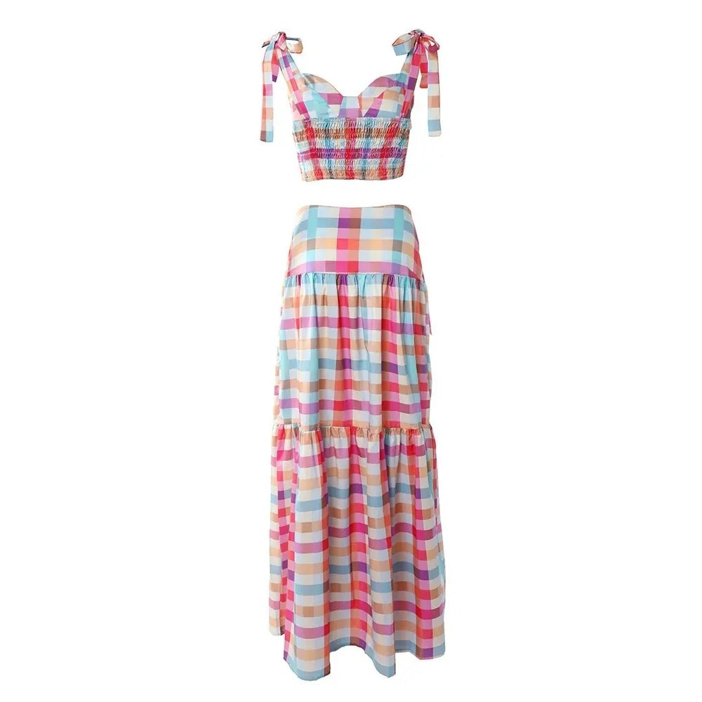 Colorful pastel checkered outfit consisting of a cropped sleeveless top with shoulder ties and a flowy tiered maxi skirt with matching pattern. Flat-lay style product shot on a plain white background, highlighting the vibrant multicolored plaid design and ruffled details.