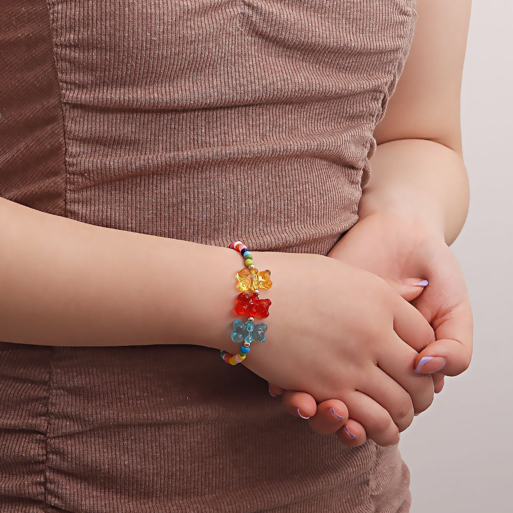Colorful beaded bracelet with multicolored seed beads and vibrant translucent gummy bear charms in yellow, red, and blue. Shown worn on a wrist with hands gently clasped, highlighting its playful and fun summer jewelry style.