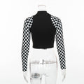 Back view of a black long-sleeve crop top on a transparent mannequin. The top features a solid black body with a high mock neck and bold black-and-white checkerboard pattern on the sleeves.