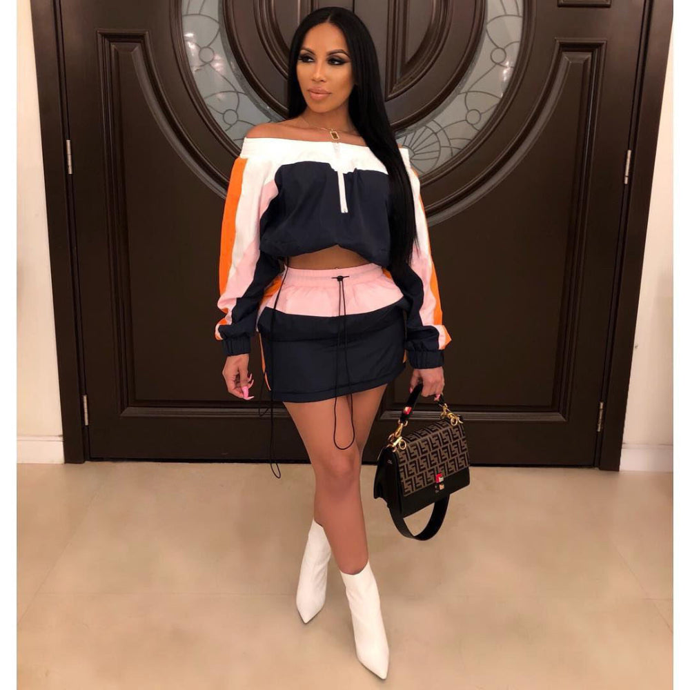 Woman in navy, orange, and pink colorblock off-shoulder crop sweatshirt and black mini skirt set with white boots, holding designer handbag.