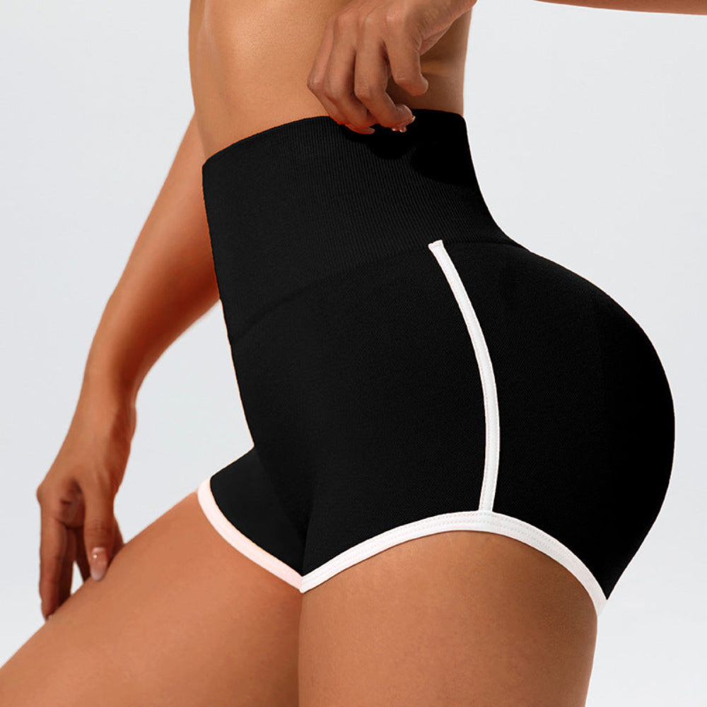 Woman modeling black high-waisted shapewear shorts with white contrast trim, shown from a rear three-quarter view against a light studio background.