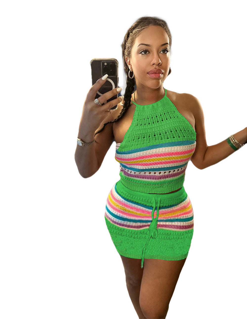 Model in a vibrant green-based multicolored striped crochet two-piece outfit featuring a halter-neck crop top and high-waisted mini skirt with drawstring detail. Full-body pose holding a smartphone for a selfie, showcasing the textured knit fabric and bright rainbow stripes on a clean white background.