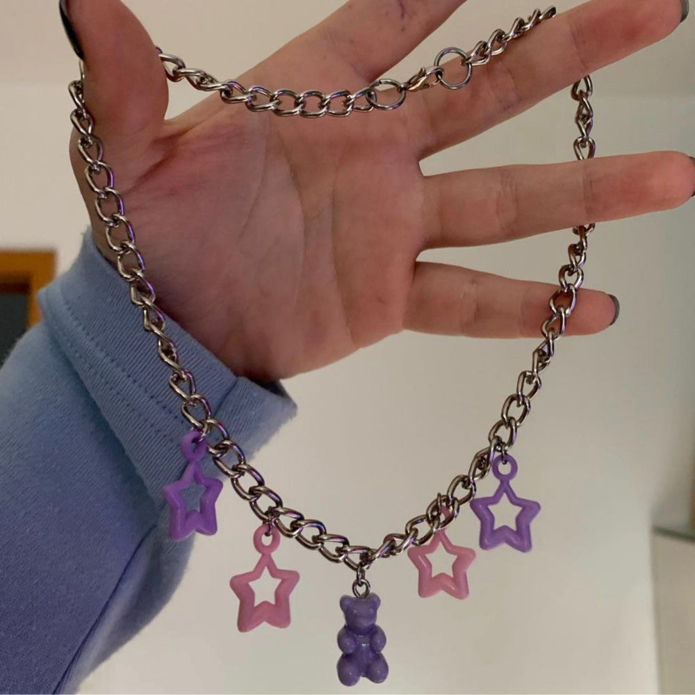 Silver curb chain necklace with playful pastel charms: purple and pink star pendants paired with a purple gummy bear charm. Featuring  the chunky chain and dangling details, creating a fun and trendy Y2K-style statement piece.