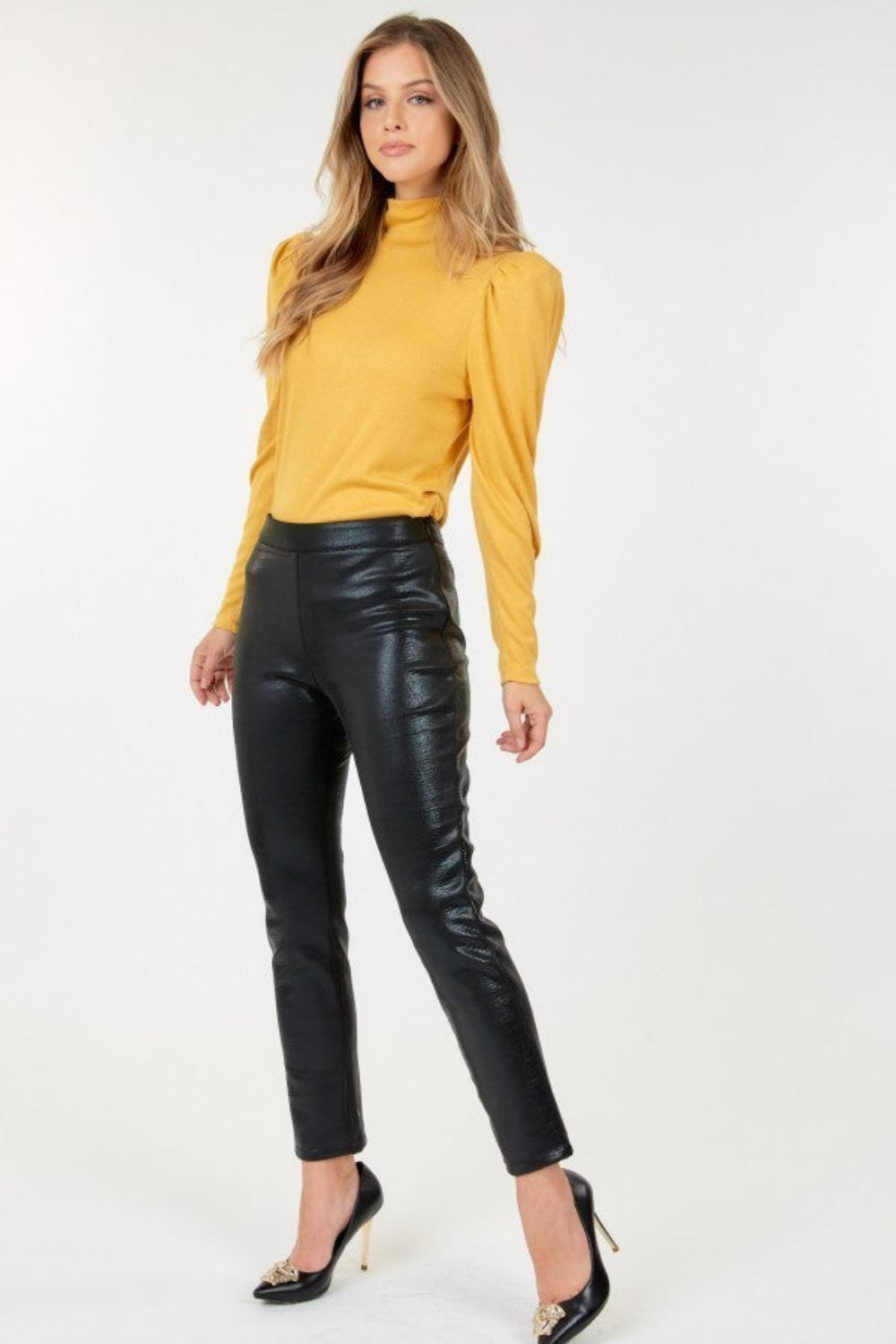 Woman wearing a yellow top and black leather pants on a white background
