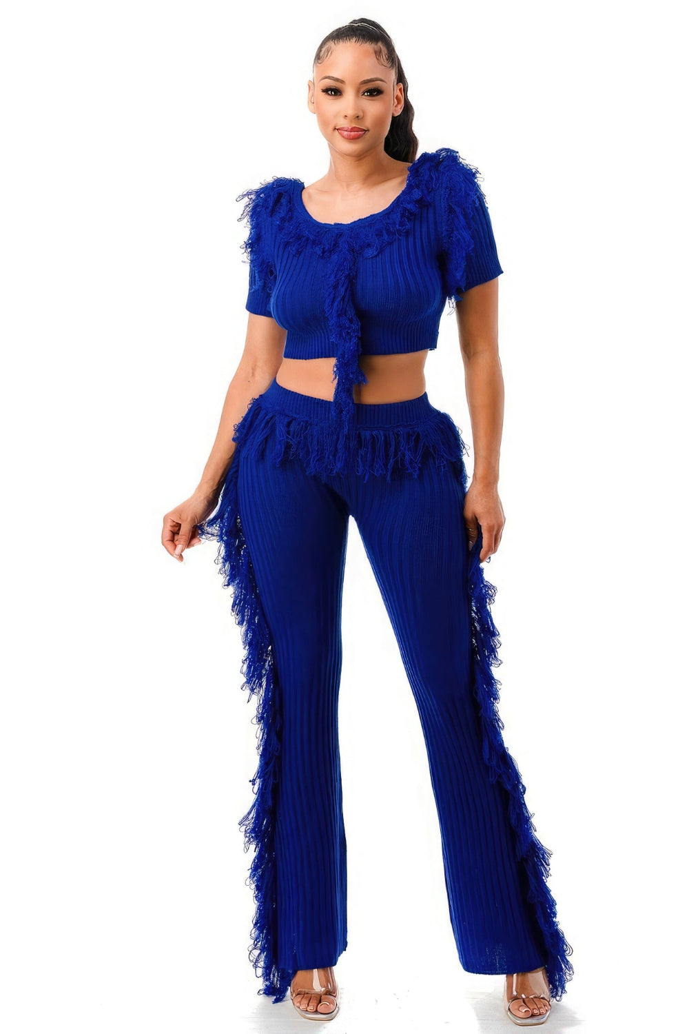 Woman wearing a royal blue ribbed knit two-piece set with a short-sleeve crop top and flare pants trimmed in feathers, paired with nude heels.