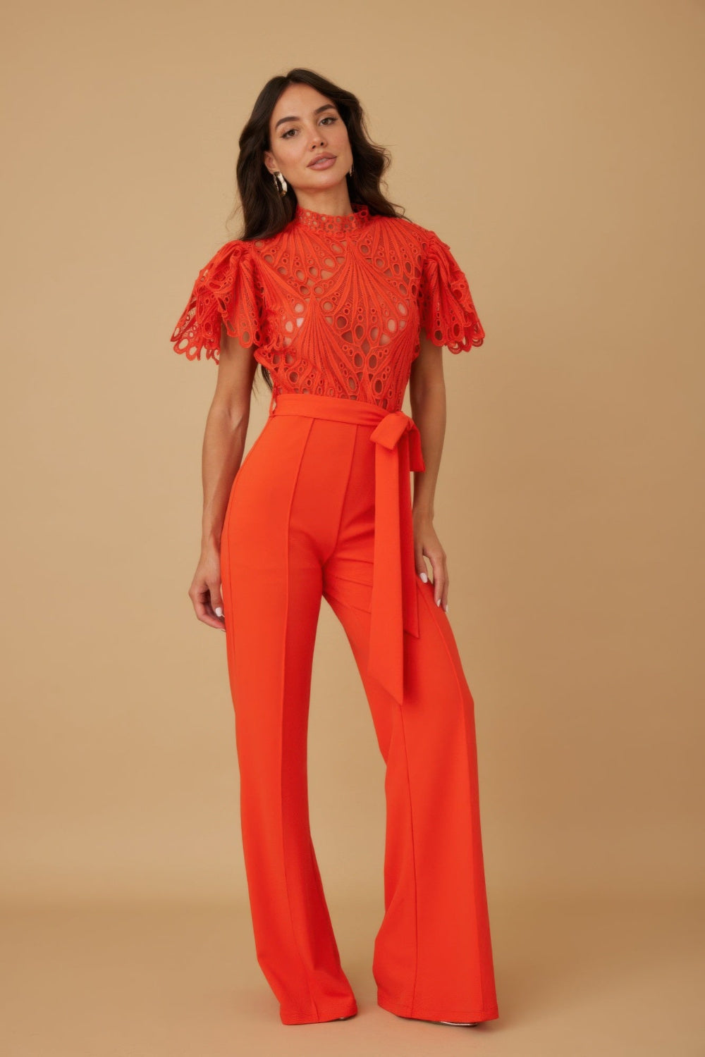 Woman wearing a red outfit with ruffled top and wide-leg pants on a beige background
