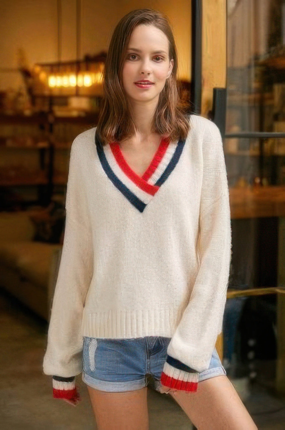 Woman wearing a cream sweater with red and blue accents in an indoor setting